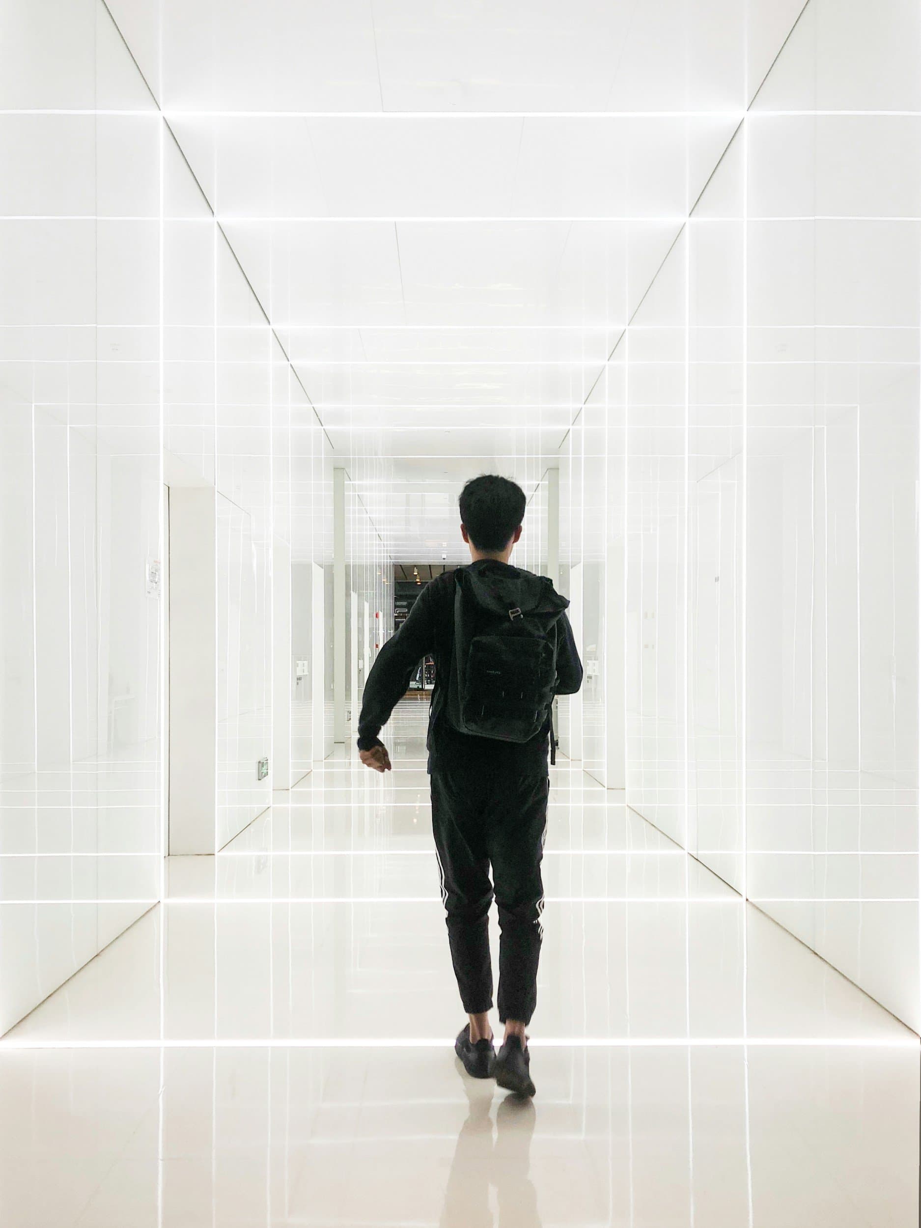 A figure walks forward through a luminous white corridor